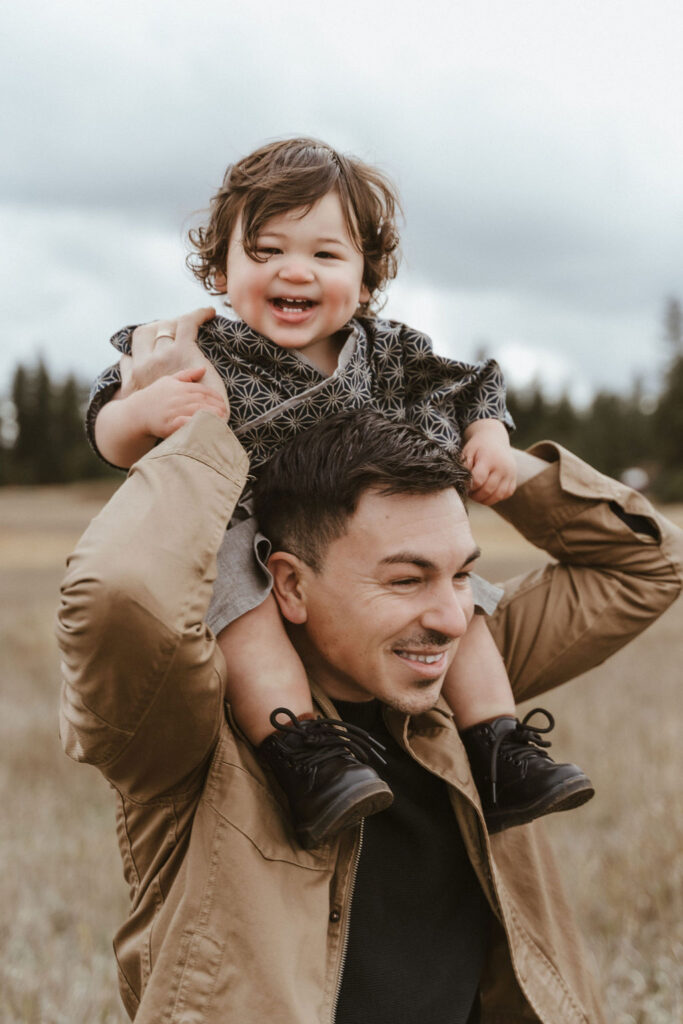 Toddler looks at the camera on top of dad's shoulders during a family photo session in Spokane, WA