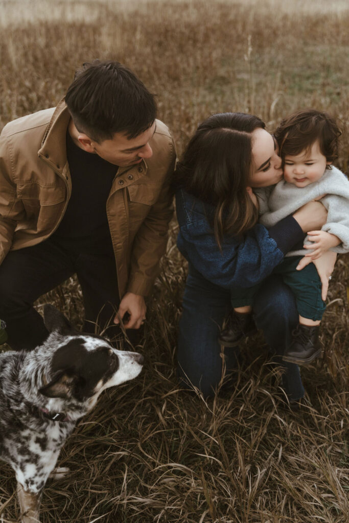 A soulful moment of this sweet family, while mom is kissing her son, dad and their family dog, Stevie, looks at them, during a Spokane family photo session with Sophie Grace Photography