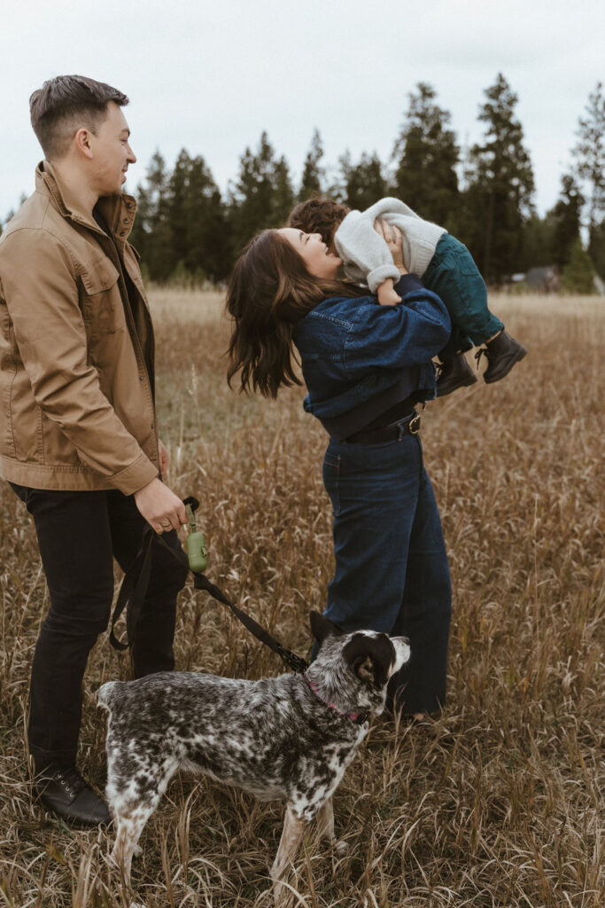 Mom tossing the baby boy in the air as dad and family dog looks at their in a fun interaction during a Spokane family photo session with Sophie Grace Photography