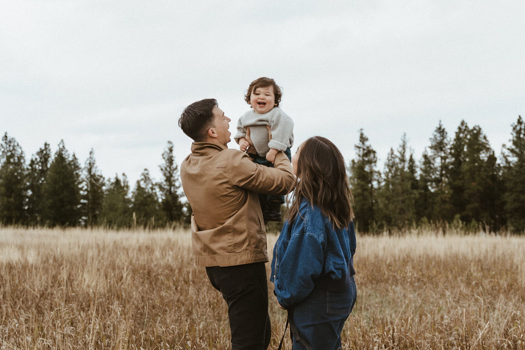 Mom and dad lifting their son up in the air, causing him to laugh, in a Spokane family photo session with Sophie Grace Photography