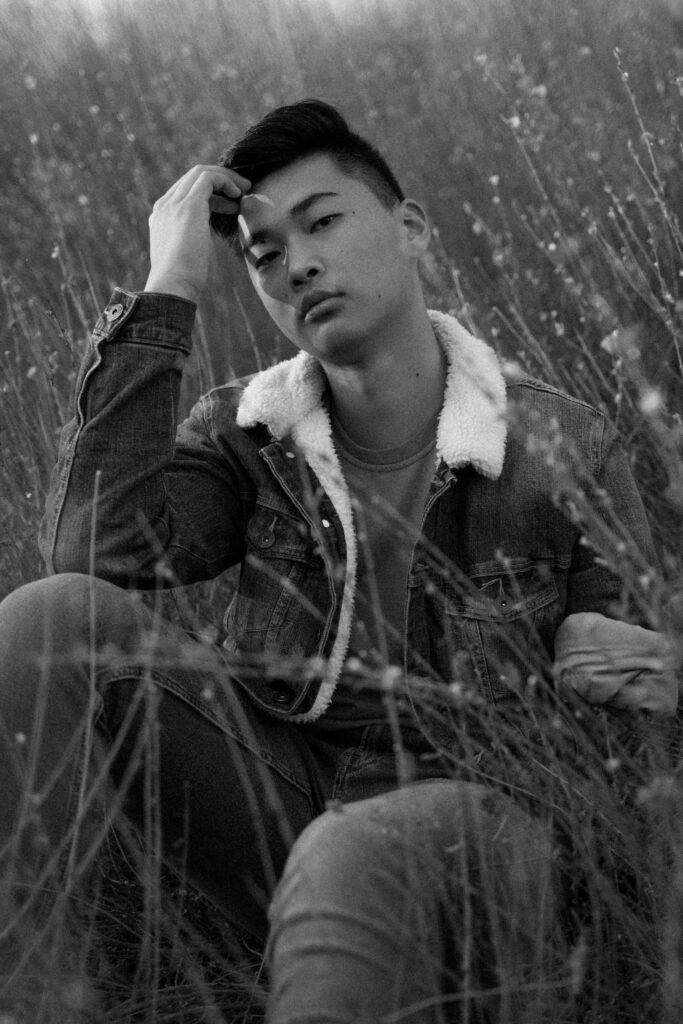 High School Senior Boy Wearing denim jacket posing in a field with Sophie Grace Photography