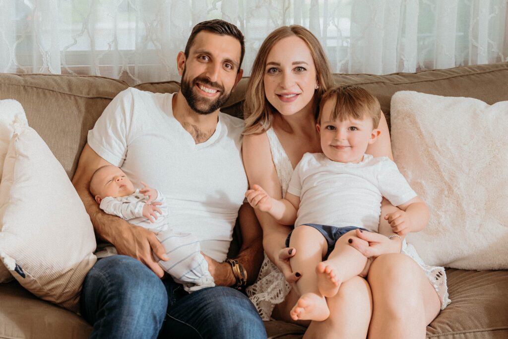 smiling family photo from mom, dad, toddler, and baby in a relaxing in home session with sophie grace photography in spokane wa