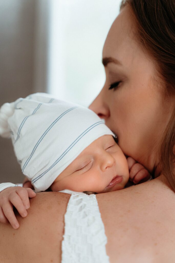 cute little face resting on mom's shoulders as she kisses his cheek in a relaxing in home session with sophie grace photography in spokane wa