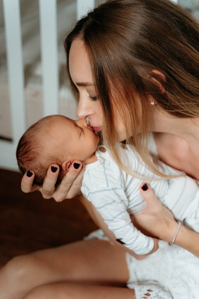 Mom kissing baby on the lips next to the crib in a relaxing in home newborn session with sophie grace photography in spokane wa