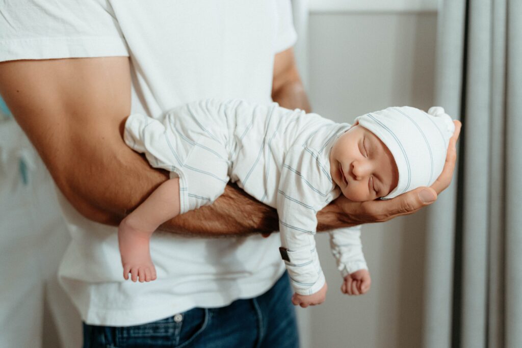 Cute baby being held in one arm by dad in a relaxing in home newborn photography in spokane with sophie grace photography