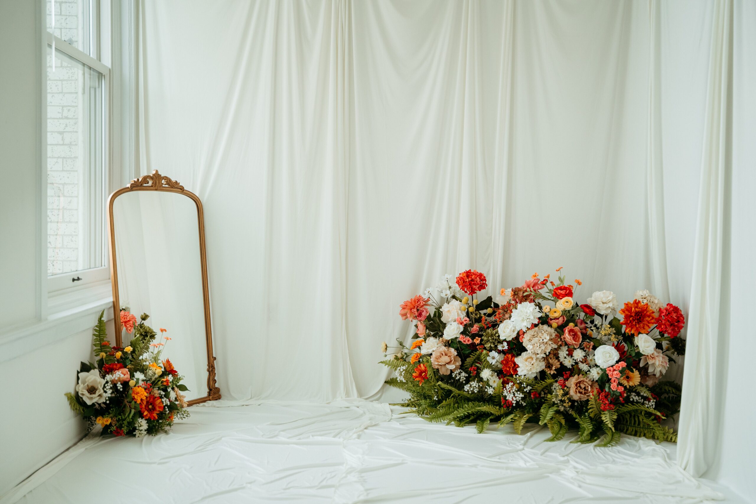 Spokane studio prepared for spring motherhood sessions with neutral draping, ornate mirror, and layered floral arrangements.